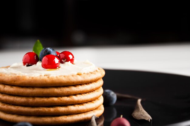 Photo cookies with cream cheese and blueberries in a dark plate surrounded with berries and dry leaves