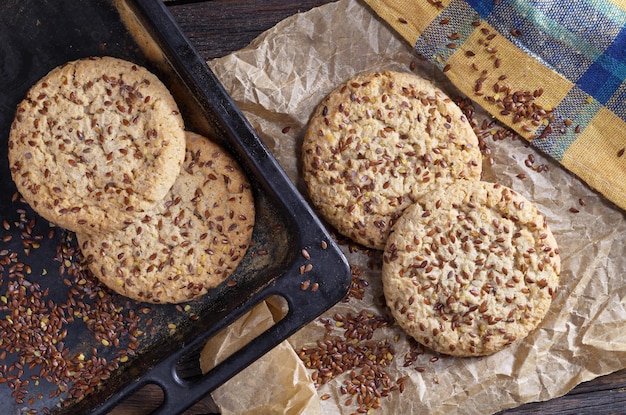 Cookies with flax seeds and sesame on baking tray on rustic wooden table with paper and napkin, top view