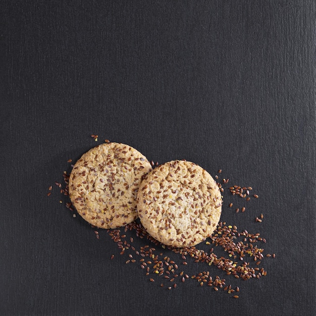 Cookies with flaxseeds and sesame on black stone background, top view with space for text
