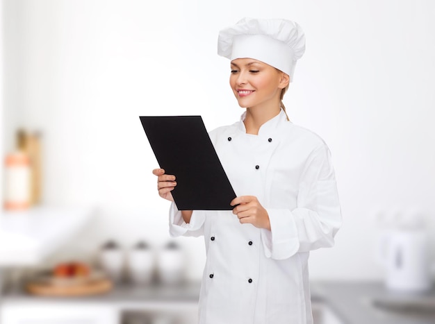 料理、広告、食品のコンセプト-笑顔の女性シェフ、空白の黒いメニュー用紙で料理人またはパン屋