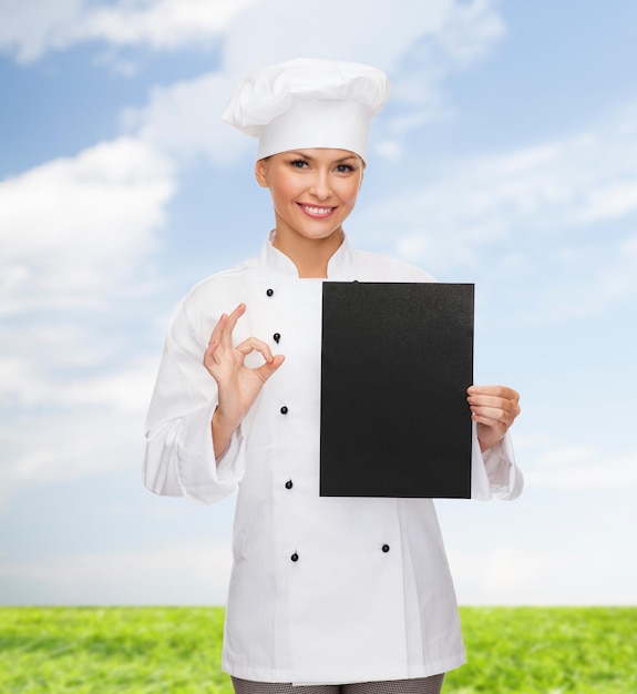 кулинария, реклама и концепция питания - улыбающаяся женщина-шеф-повар, повар или пекарь с чистой черной бумагой, показывающей хорошо петь