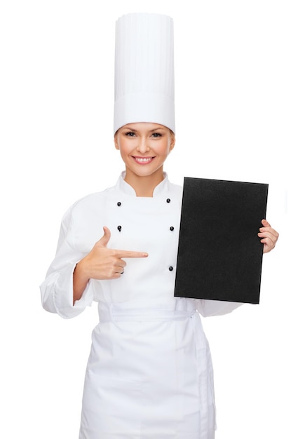 cooking, advertisement and food concept - smiling female chef pointing finger to blank black paper