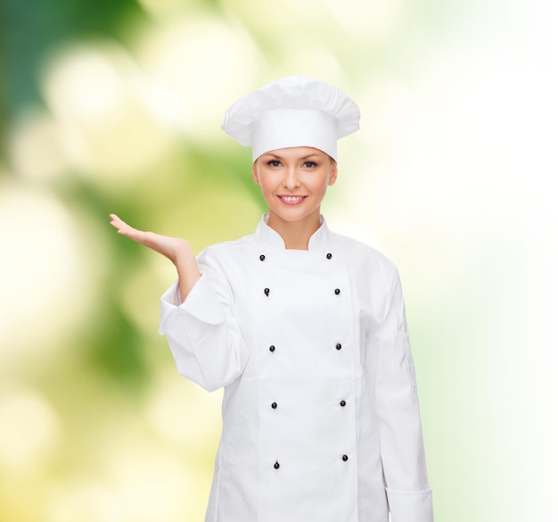 cooking, advertisement and people concept - smiling female chef, cook or baker holding something on palm of hand over green background