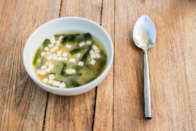 cooking, asian kitchen and food concept - bowl of soup with tofu cheese and spoon on wooden table