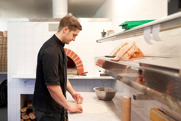 cooking, baking and people concept - chef preparing dough for pizza in kitchen at pizzeria