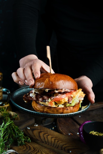 調理。シェフの手にベーコンとエビを添えたハンバーガー。暗い背景に。