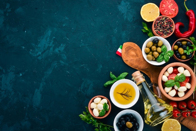 Cooking a caprese salad Mozzarella cheese cherry tomatoes olives basil leaves oil pepper On a black stone table Free space for text