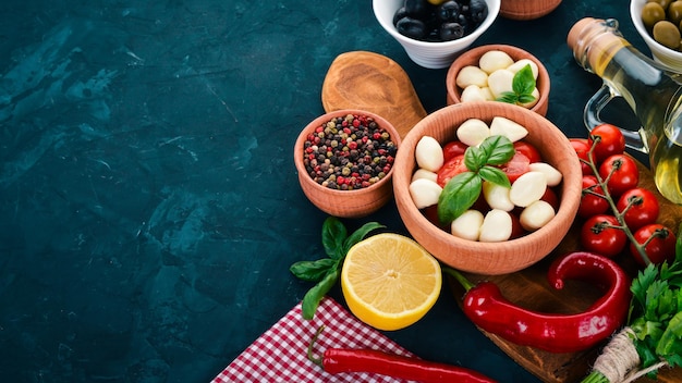 Cooking a caprese salad Mozzarella cheese cherry tomatoes olives basil leaves oil pepper On a black stone table Free space for text