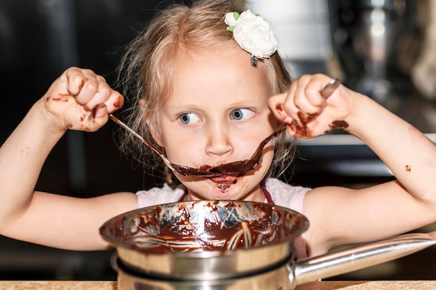 チョコレートを調理する小さな女の子子供が溶けたチョコレートをなめるパティシエ子供クッキンで楽しんで