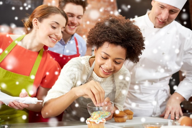 Photo cooking class, culinary, bakery, food and people concept - happy group of friends and male chef cook baking in kitchen over snow effect