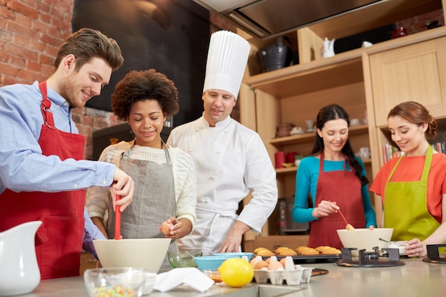 cooking class, culinary, bakery, food and people concept - happy group of friends and male chef cook baking in kitchen