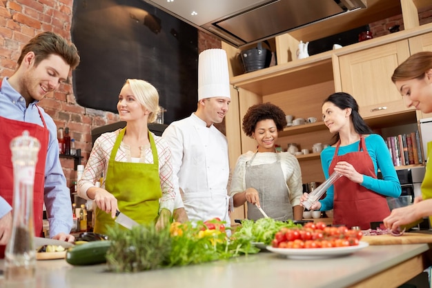 Photo cooking class, culinary, food and people concept - happy group of friends with male chef cook cooking and talking in kitchen