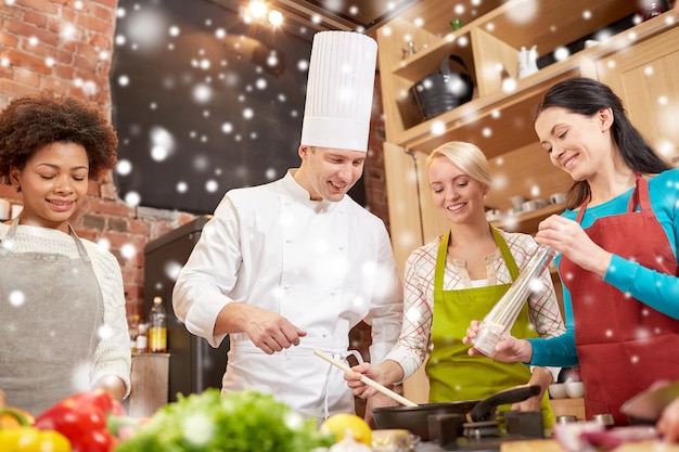 Photo cooking class, culinary, food and people concept - happy group of women and male chef cook cooking in kitchen over snow effect