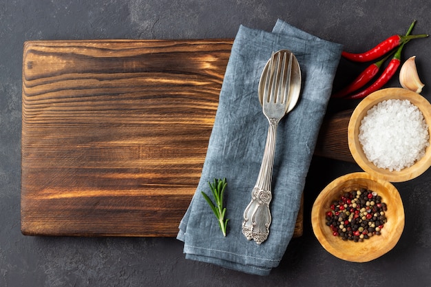 Cooking concept. Vintage cutting board with spices and cutlery on dark stone background. Copy space.