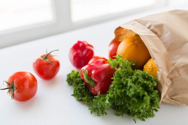 кулинария, диета, вегетарианская еда и концепция здорового питания - крупный план бумажного пакета со свежими спелыми сочными овощами и зеленью на кухонном столе дома
