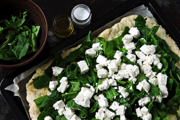 Cooking feta spinach pizza. Keto pizza. Raw feta spinach pizza on a sheet for baking. Flat lay.