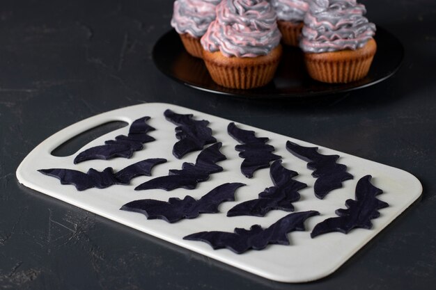 할로윈 파티를 위해 컵케이크를 장식하기 위해 검은 매스틱으로 박쥐를 요리합니다. 확대