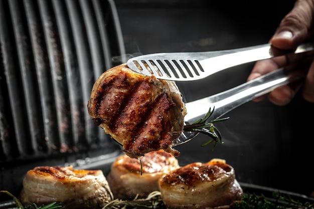 Photo cooking fillet mignon on grill by chef hands. tenderloin meat beef steaks fillet wrapped in bacon. food recipe background. close up