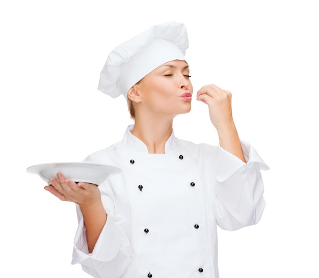 cooking and food concept - smiling female chef, cook or baker with empty plate showing delicious sign