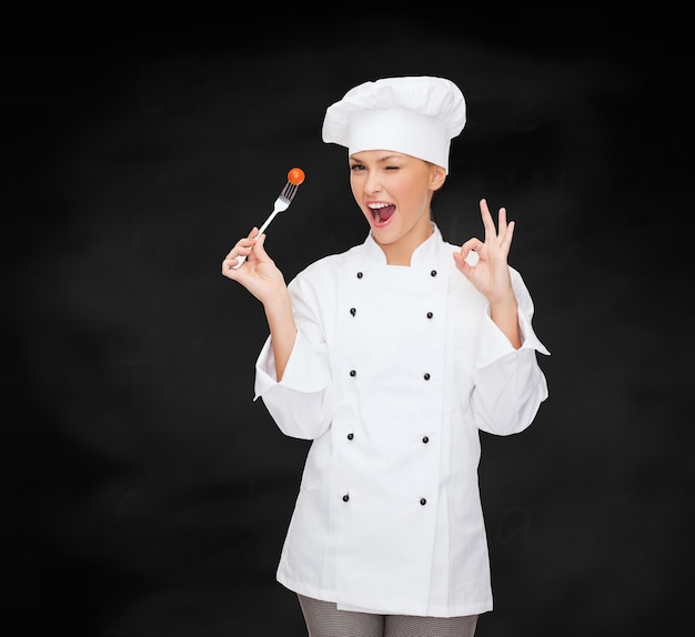 cooking and food concept - smiling female chef, cook or baker with fork and tomato showing ok sign