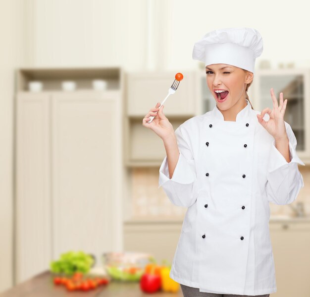 концепция кулинарии и еды - улыбающаяся женщина-повар, повар или пекарь с вилкой и помидором, показывающая знак ок