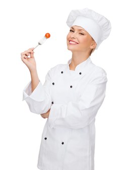 Concetto di cucina e cibo - chef femminile sorridente, cuoco o fornaio con forchetta e pomodoro