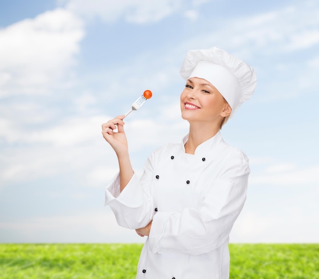 концепция кулинарии и еды - улыбающаяся женщина-повар, повар или пекарь с вилкой и помидорами