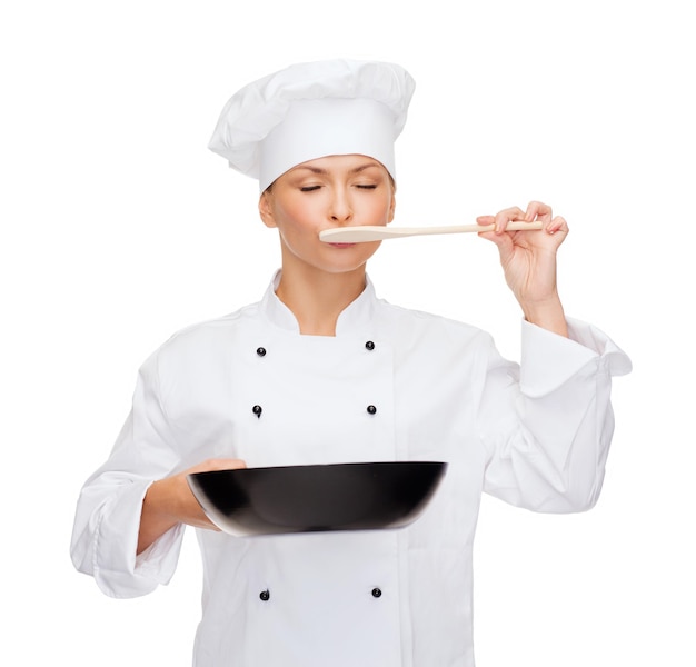 cooking and food concept - smiling female chef, cook or baker with pan and spoon tasting food