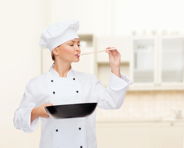 cooking and food concept - smiling female chef, cook or baker with pan and spoon tasting food