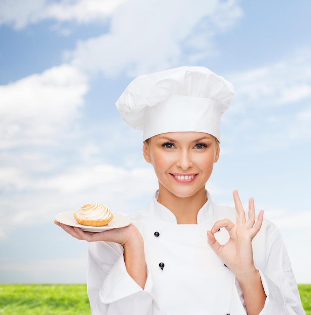 Concetto di cucina e cibo - chef femminile sorridente, cuoco o fornaio con torta sul piatto e segno ok Foto Premium