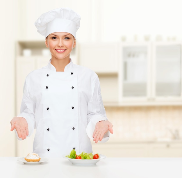 cooking and food concept - smiling female chef, cook or baker with salad and cake on plates