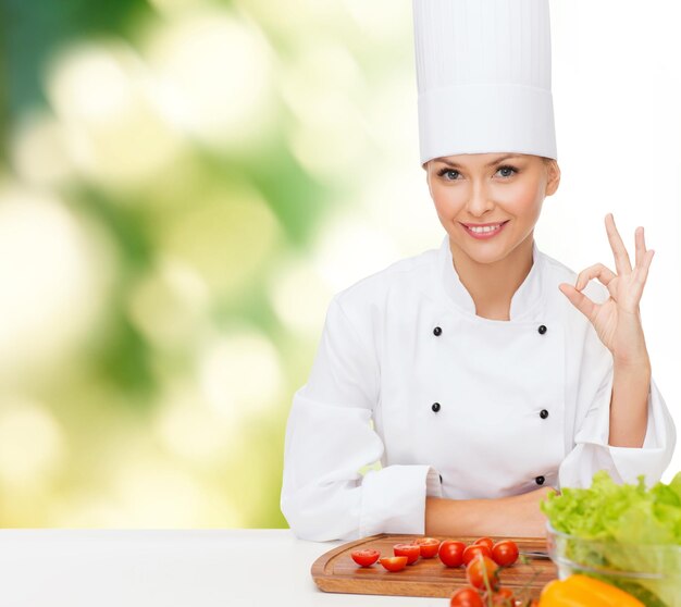 Concetto di cucina e cibo - chef femminile sorridente con verdure che mostrano segno ok