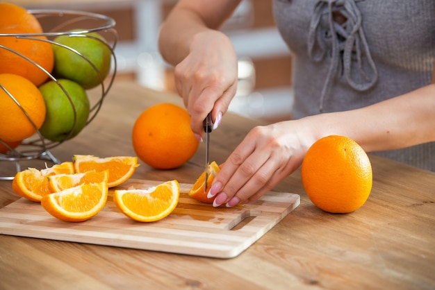Foto cucinare il cibo e il concetto di vigore del veganismo e mangiare sano primo piano della mano femminile che taglia l'arancia a fette