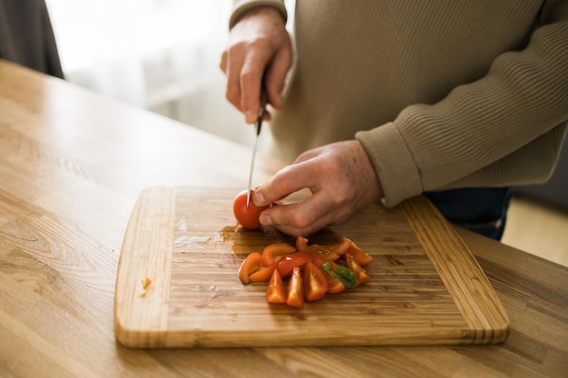 料理と家庭のコンセプトは、自宅のまな板の上でトマトを切る男性の手の接写