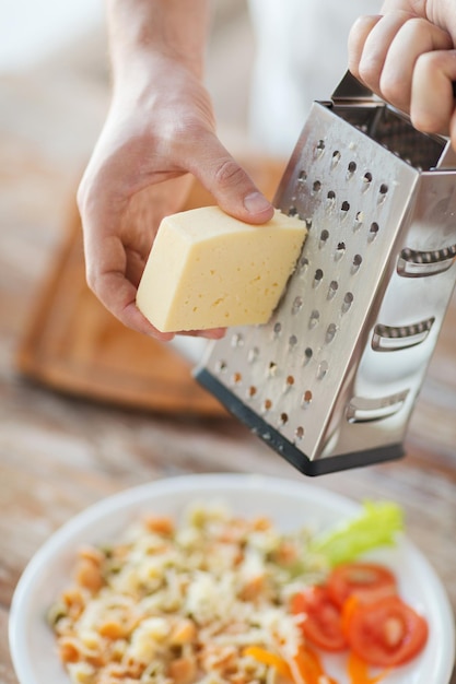 料理、食べ物、家庭のコンセプト-パスタの上にチーズをすりおろす男性の手のクローズアップ