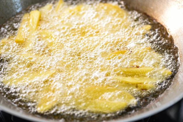 Cooking french fries or fry potatoes in hot oil for potato wedges Close up fried potatoes in oil on pan