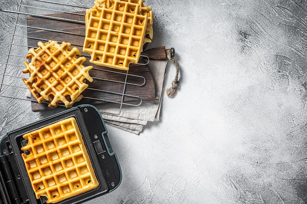 Cooking of fresh waffles in waffle maker. White background. Top view. Copy space.