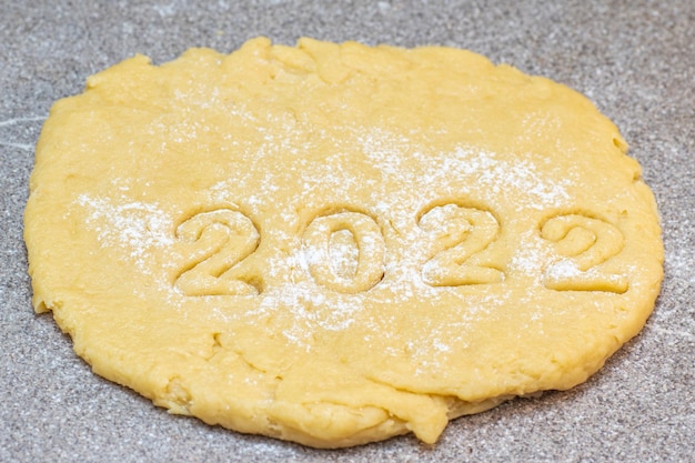 Cooking gingerbread cookies from raw dough sprinkled with flour with the numbers of the year 2022 for cookies.