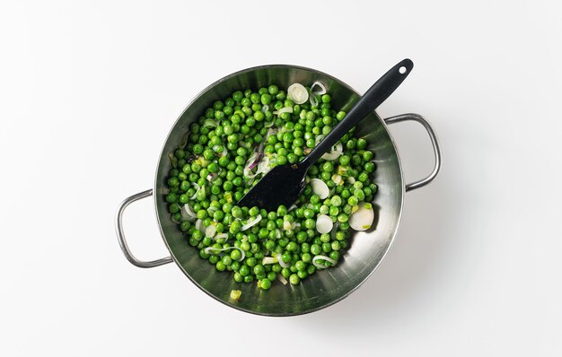 Foto cucinare i piselli con le cipolle verdi in una padella. ricetta primaverile