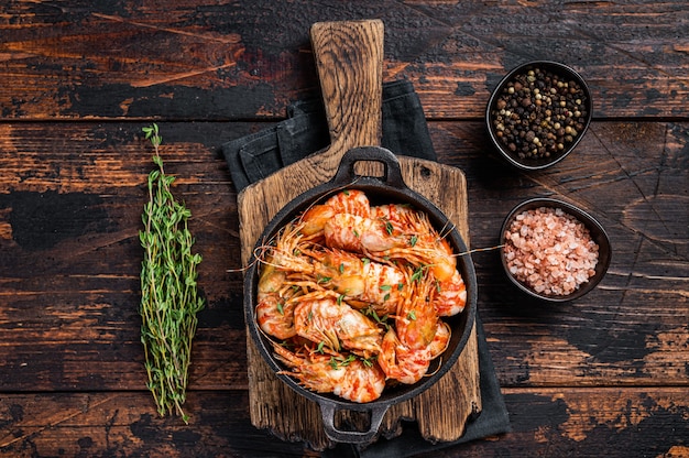 Cooking Greenland Shrimps Prawns in a pan with thyme and rosemary. Dark wooden background. Top view.