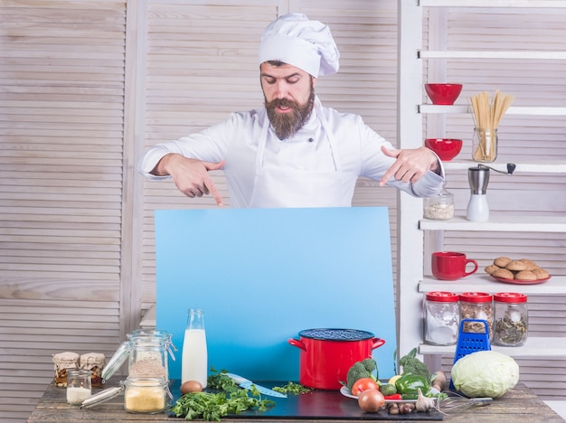 Cooking handsome bearded chef in uniform ingredients professional kitchen chef holds advertising