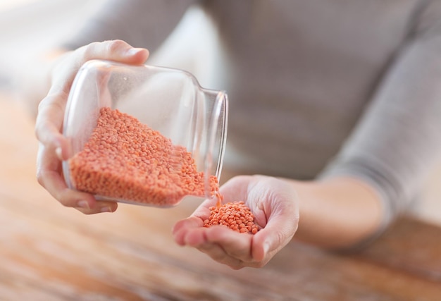 cooking and home concept - close up of female emptying jar with red lentils