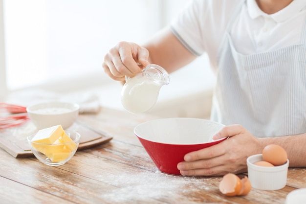 cooking and home concept - close up of male hand pouring milk in bowl