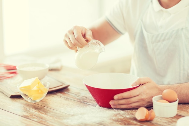 cooking and home concept - close up of male hand pouring milk in bowl