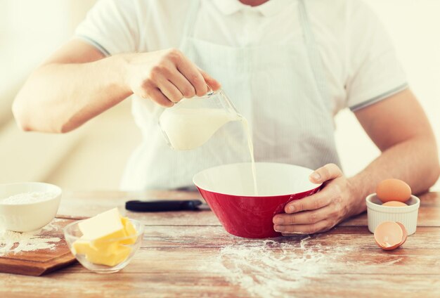 cooking and home concept - close up of male hand pouring milk in bowl