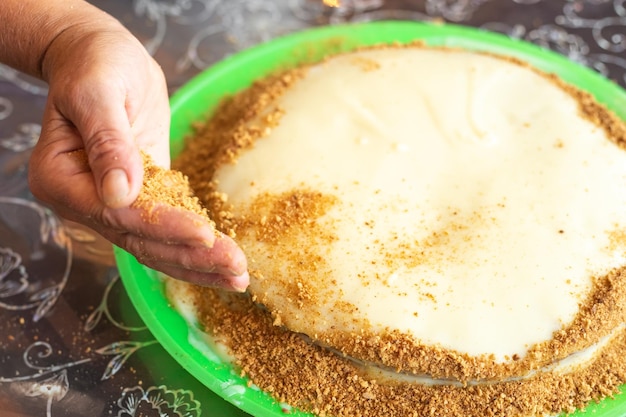 Cooking homemade cake A woman sprinkles a baked and creamcovered cake with confectionery crumbs