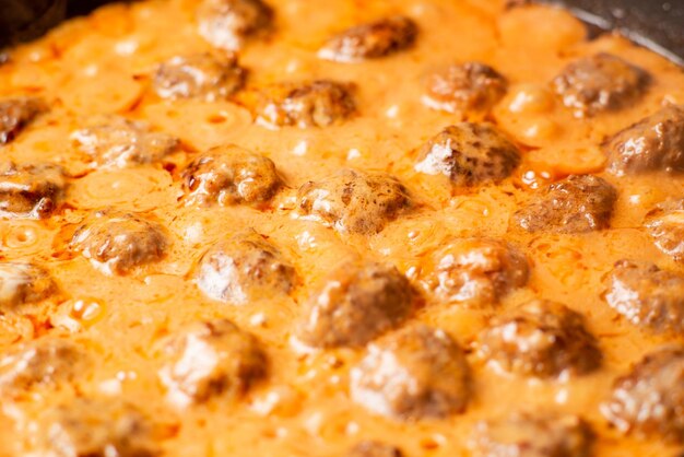 Cooking homemade meatballs in a frying pan in a sauce of tomatoes and sour cream Closeup macro Food background