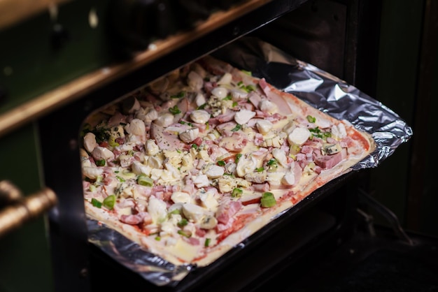 Cooking homemade pizza on a baking sheet in the oven Pizza with mozzarella cheese herbs and ham