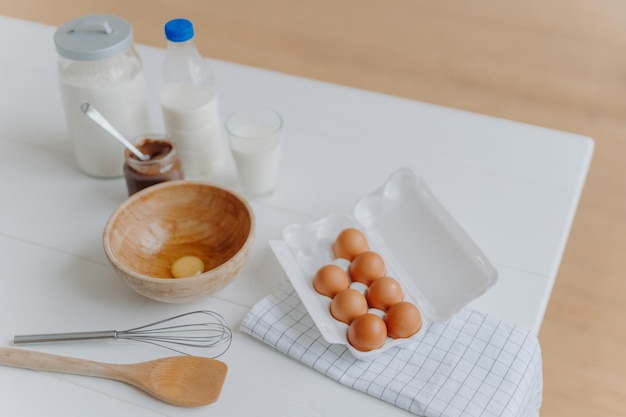 Cooking ingredients on kitchen table View from above of eggs milk and flour whisk and wooden spatula near Utensils and fresh products