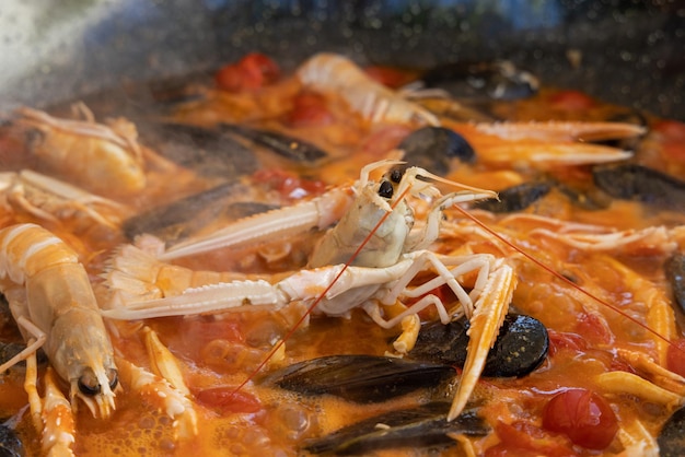 Cooking Italian stew with seafood and tomatoes in a big frying pan close up